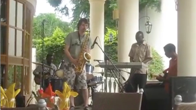 Man convinces African jazz band he can play the saxophone. He really, really can’t