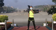 Exercise instructor does aerobics class while military coup takes place behind her