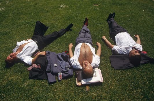 Looking down from above, we see young men who are open-chested and with their suit jackets either beneath their heads or on the grass, three office co-workers stretch out over the lush grass and sunbathe during a hot summer lunchtime in Trinity Square in the City of London, England. One has his paperwork under his head and a can of Coke to quench his thirst. Already tanned, the threesome bask under a hot mid-day sun. Risking sunburn after prolonged solar radiation exposure, they enjoy the inner-city heatwave. (Photo by In Pictures Ltd./Corbis via Getty Images)