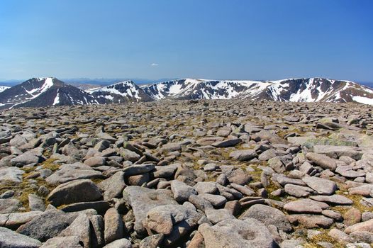 Boulders and rocks on the summit of Ben Macdui with snow-covered mountain ridge in the background stock photo